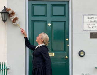 A lady in Victorian costume is standing outside the front door of 4, Clarence Road. She is dusting the lamp with a feather duster so the museum is ready for visitors