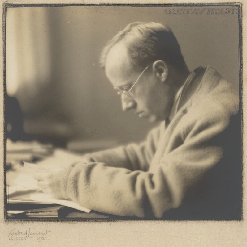 A sepia image of Gustav Holst reading papers at a desk